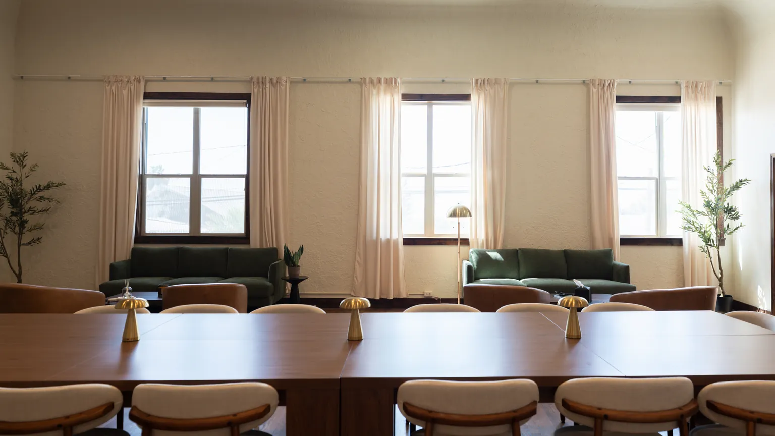 The Colab's main room in downtown Exeter: the long walnut table with brass lamps, and green sofas and leather chairs under three tall curtained windows.